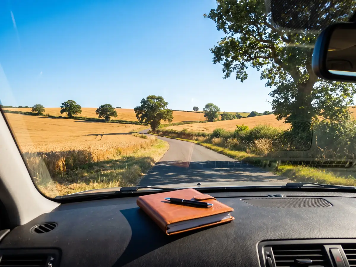 A mileage log book and pen on a car dashboard, the contemporaneous record behind a business mileage claim.